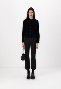 Must või musta sametist nööbipaneeliga särk, mille juurde on sobitatud kõrge vöökohaga mustad püksid. Aksessuaarideks on väike must kott ketist rihmaga.