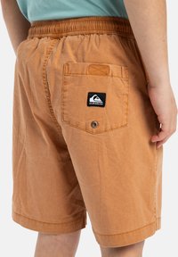 Oranžové bavlněné kraťasy s elastickým pasem, bočními kapsami a jednou zadní kapsou s černou nášivkou loga Quiksilver.