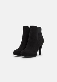 Bottines en daim noir avec un talon haut, un bout arrondi et des panneaux latéraux élastiques pour un enfilage facile. Texture lisse sans motifs visibles.