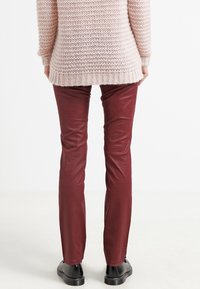 Mörkröda läderbyxor med en figurnära design, som har en slät yta och raka ben, tillsammans med en ljusrosa stickad tröja.