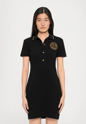 Black polo dress with short sleeves, gold accent stitching, and a circular logo patch on the left chest. Soft, smooth fabric.