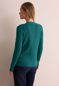 Türkiser, gerippter Pullover mit langen Ärmeln und Rundhalsausschnitt, der eng anliegt und aus strukturiertem Stoff gefertigt ist, kombiniert mit dunklen Jeans.