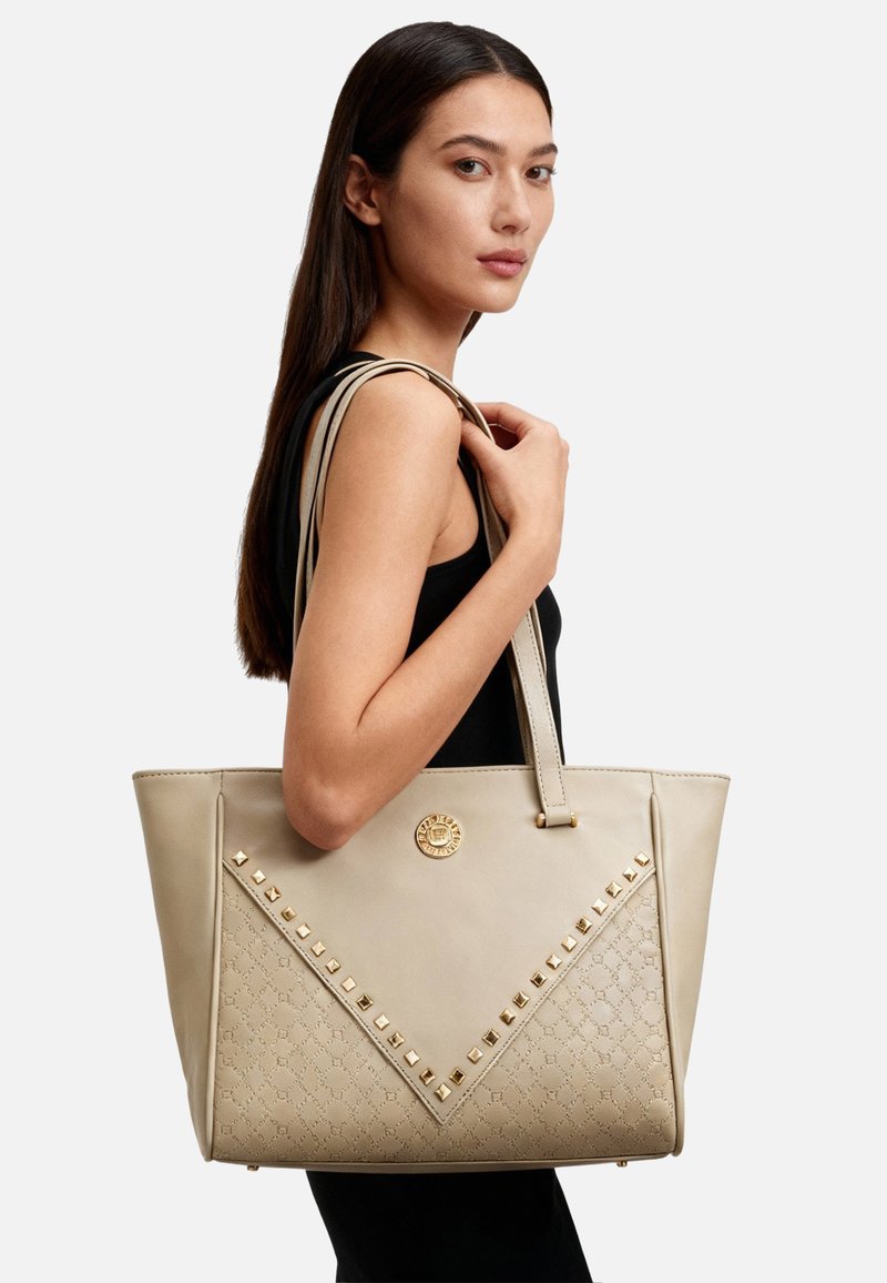 Borsa tote beige con texture in pelle liscia, design triangolare, borchie color oro sulla parte anteriore e un emblema con il logo. Due manici lunghi.