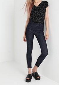 Black short-sleeve top with a geometric pattern, paired with dark denim skinny jeans featuring a side stripe and black platform sandals.