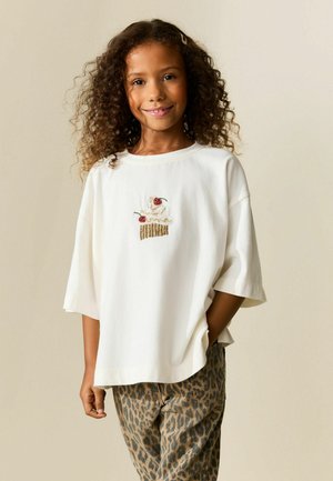 Hvid T-shirt med korte ærmer med farverigt cupcake-broderi på brystet. Kombineret med beige bukser med leopardprint. Glat tekstur.