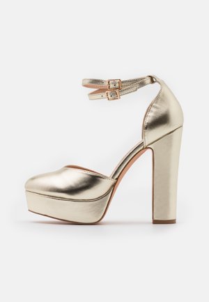 Goldfarbene, metallische High-Heel-Plateauschuhe mit runder Zehenpartie, Fesselriemen mit doppelten Schnallen und strukturierter Oberfläche.