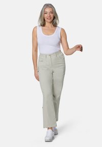 Hellebeige Cargo-Hosen mit Fronttaschen, einem lockeren Schnitt und einem elastischen Bund, kombiniert mit einem weißen ärmellosen Top und weißen Schuhen.