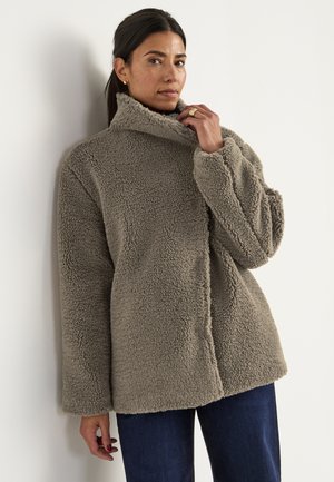 Flauschige beige Fleecejacke mit hohem Kragen, lässiger Passform und langen Ärmeln. Hat eine glatte Textur und keine sichtbaren Verschlüsse.