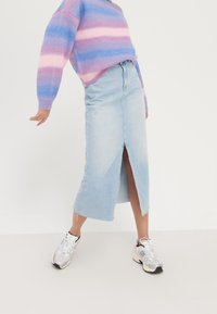 Jupe midi en jean bleu clair avec une fente à l'avant et un ourlet effiloché, associée à un pull en maille rayé multicolore et des baskets grises.