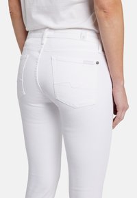Jeans in denim bianco con un design aderente. Presentano tasche posteriori con dettagli di cucitura e un piccolo bottone metallico sulla vita.