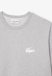 Szürke pulóver pamut keverékből, kerek nyakkivágással, hosszú ujjakkal, bal mellkason fehér krokodil logóval.