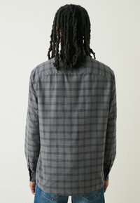 Camicia a quadri grigia con colletto button-down, maniche lunghe e orlo leggermente curvato. La trama del tessuto è morbida con una finitura liscia.