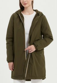 Veste matelassée vert olive avec fermeture éclair à l'avant, capuche, poignets élastiques et poches latérales. Intérieur doublé d'un tissu doux et texturé.