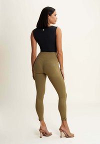 Top senza maniche nero abbinato a leggings a vita alta verde oliva. I leggings presentano cuciture curve e una trama di tessuto liscia e elastica.