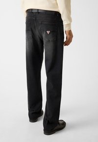 Jean en denim noir avec finition délavée. Présente un logo triangulaire sur la poche arrière, une coupe droite et des détails de coutures discrètes.