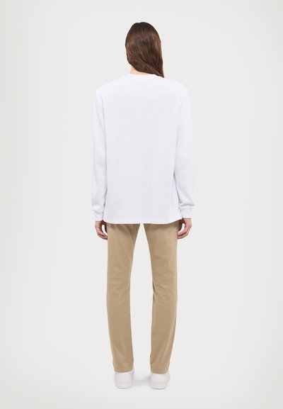 White long-sleeve shirt with a rounded neckline, paired with beige straight-leg pants. The fabric appears smooth with subtle texture.