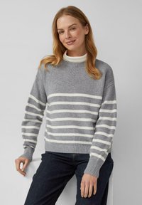 Grau gestreifter Pullover mit weißen horizontalen Streifen, gerippten Bündchen und Saum, runder Ausschnitt, getragen über einem weißen Rollkragenpullover, kombiniert mit dunklen Jeans.