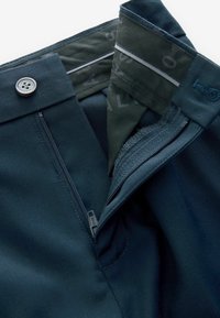 Laivastonsiniset housut, joissa on metallinen nappi, vetoketjullinen etumelu, sekä sisäkaarre, jossa on kontrastivärinen kangas ja logopainatus. Sileä pinta.