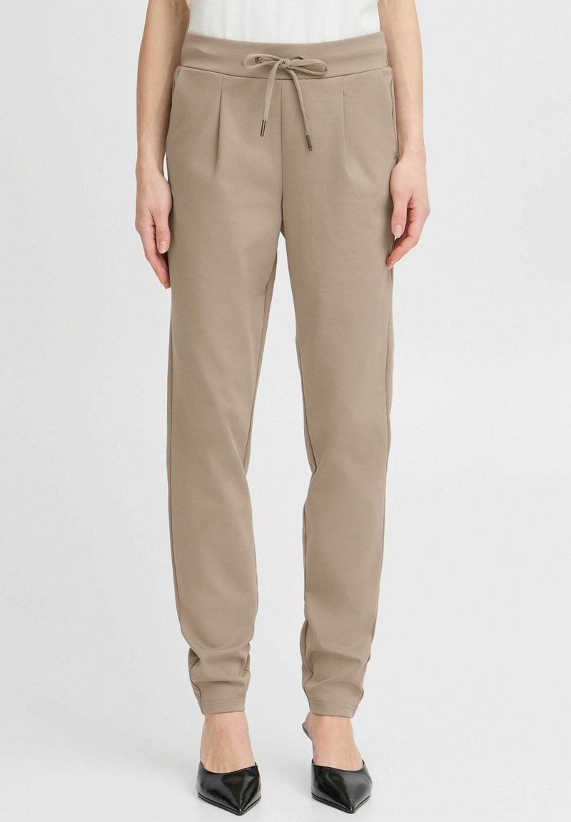 Beiga sweatpants med snörning i midjan, veckad front och tapered ben-design. Slät tygtextur, kombinerad med spetsiga svarta klackar.
