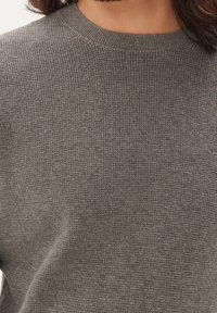Szary sweter dziany z teksturowaną powierzchnią i prążkowanym dekoltem, o luźnym kroju i miękkim materiale. Brak widocznych szwów i ozdób.