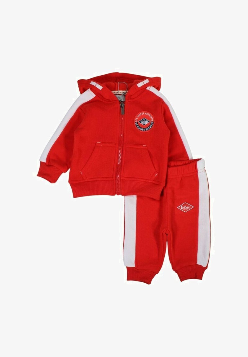 Survêtement rouge avec bandes blanches latérales, sweat à capuche zippé avec deux poches avant et un logo rond, pantalon assorti avec taille élastique et ourlets côtelés.