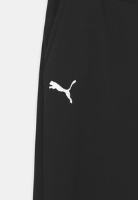 Pantalones deportivos negros hechos de una tela texturizada con un logo blanco de Puma en el muslo. Diseño simple sin patrones o acentos adicionales.