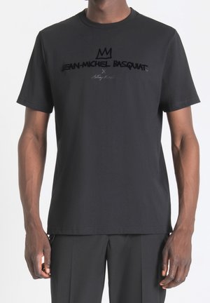 Mann trägt schwarzes T-Shirt mit schwarzem Kronenlogo und dem Text „Jean-Michel Basquiat x Antony Morato“ in der Mitte der Brust.