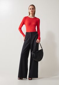Red long-sleeve bodysuit paired with black wide-leg trousers. Model holds a black bag with curved design and braided handle.