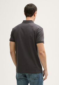 Polo gris au design simple, à manches courtes et col à deux boutons. Tissu en coton. Porté avec un jean en denim bleu.