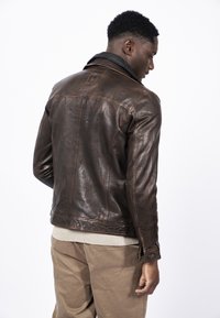 Chaqueta de cuero marrón con un cuello negro, costuras visibles y un diseño ajustado. Superficie texturada con acentos envejecidos.