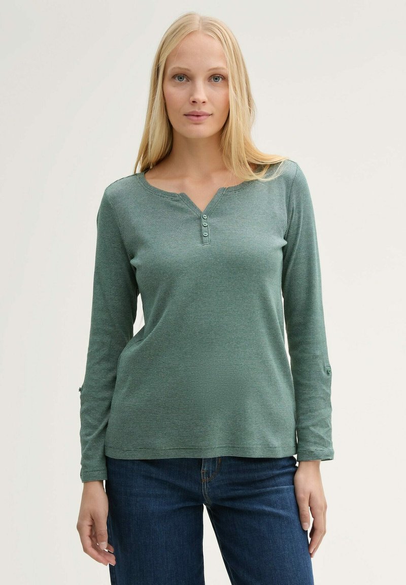 Groene longsleeve top met een henley-kraag, voorzien van een knoopsluiting en een subtiel streepjespatroon, gecombineerd met donkerblauwe jeans.