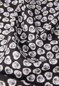 Zwarte stof met een patroon van witte harten, waarvan elk een klein gezichtontwerp bevat. De textuur lijkt glad en iets glanzend.