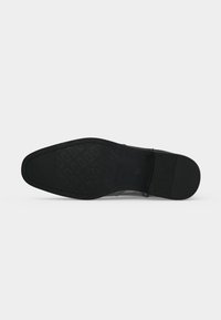 Semelle de chaussure noire avec motif de bande de roulement texturé et talon lisse, présentée à plat sur un fond clair uni.