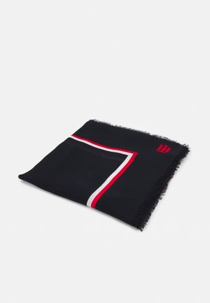 Sort foldet tørklæde med frynser på kanterne, med et hjørne i røde, hvide og sorte striber og et lille rødt broderet logo.