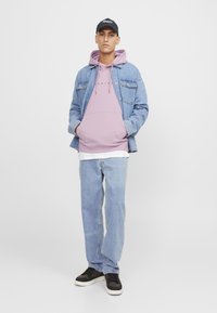 Chaqueta de mezclilla azul claro sobre una sudadera rosa, camiseta blanca y jeans azul claro. Zapatillas negras completan el atuendo. Diseño simple, ajuste casual.