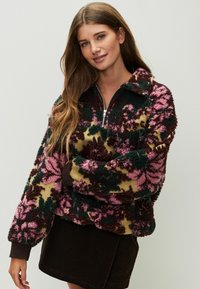 Fleecová mikina s vysokým golierom, zdobená kvetinovými vzormi v ružovej, zelenej a hnedej farbe na béžovom podklade. Zapínanie na zips a rebrované manžety.