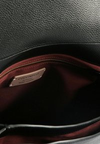 Zwarte leren handtas met een interieur van bordeauxrode voering, met een ritssluiting en een label met de tekst "Coccinelle Authentiek Italiaans Leder".