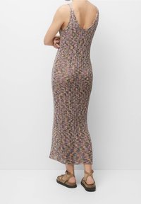 Vestido maxi de patrón de punto multicolor con tirantes finos y espalda en V. Usado con sandalias de tiras marrones. Tejido suave y texturizado.