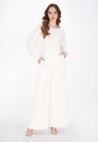 Top bianco a maniche lunghe con scollatura ampia, abbinato a pantaloni a vita alta e gamba larga. L'outfit presenta un tessuto morbido e un design minimalista.