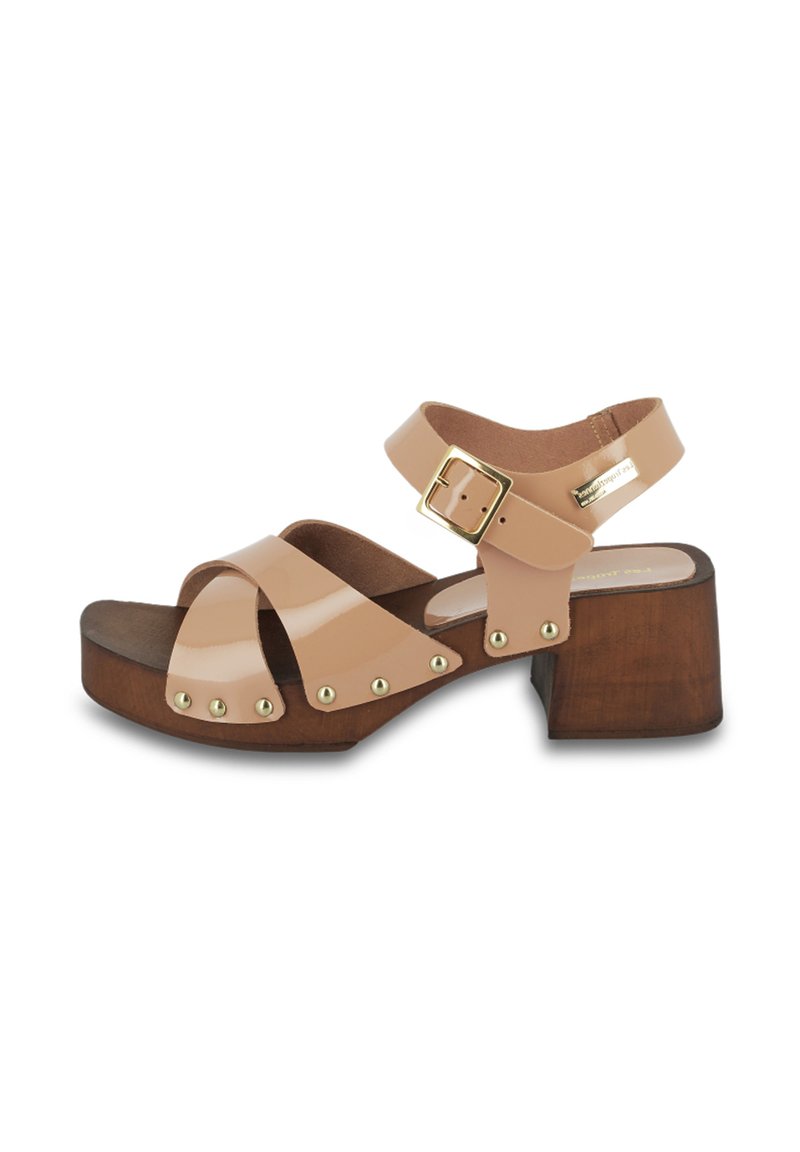 Sandal de charol beige con tres tiras, herrajes dorados y tacón de bloque de madera. Presenta clavos metálicos a lo largo de las tiras para detalle.