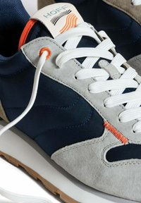 Sneaker navy e grigie con tomaia in suede e tessuto, lacci bianchi e una cucitura arancione di dettaglio. Logo "HOFF" sulla linguetta.