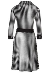 Robe à motif pied-de-poule noir et blanc, manches longues, col avec col, et une ceinture noire unie. Texture de tissu lisse.