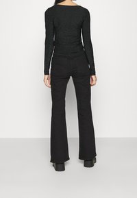 Svart långärmad topp med glittrande textur, tillsammans med högmidjade svarta utsvängda jeans. Outfitten har en figurnära passform.