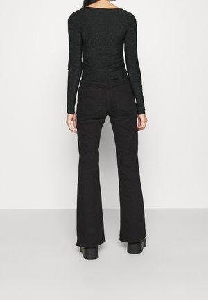 Schwarzes Langarmoberteil mit glitzernder Textur, kombiniert mit hochgeschnittenen schwarzen Schlagjeans. Das Outfit hat eine taillierte Silhouette.