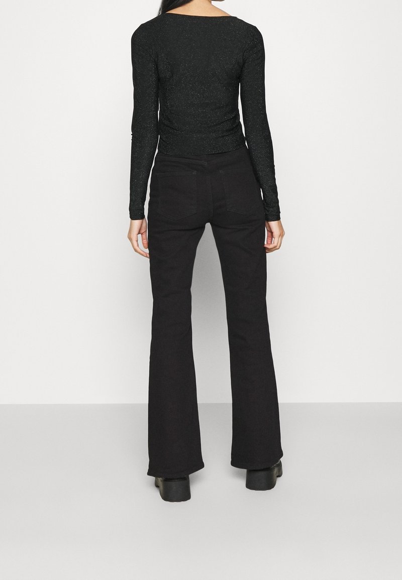 Svart långärmad topp med glittrande textur, tillsammans med högmidjade svarta utsvängda jeans. Outfitten har en figurnära passform.