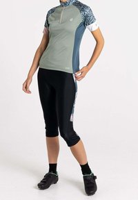 Kortärmad cykeltröja i grönt och blått med dragkedja, kombinerad med svarta caprishorts. Tröjan har färgglada mönstrade ärmar och detaljer.