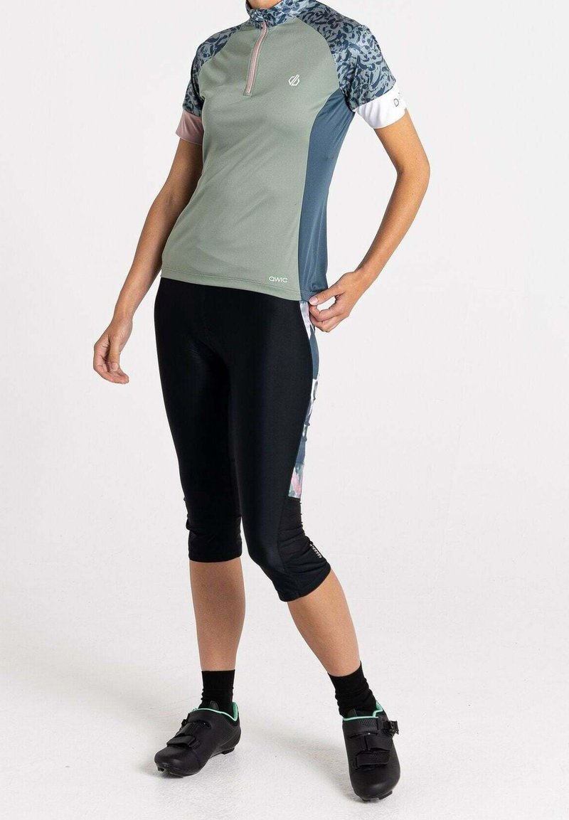 Kortärmad cykeltröja i grönt och blått med dragkedja, kombinerad med svarta caprishorts. Tröjan har färgglada mönstrade ärmar och detaljer.