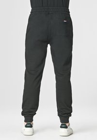 Pantaloni jogger neri con vita elastica e polsini alla caviglia. Presentano una tasca posteriore con un accento del logo del marchio. Tessuto morbido e strutturato.