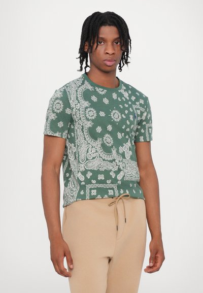 Groene katoenen t-shirt met een wit paisleypatroon en korte mouwen, gecombineerd met beige broek met trekkoord.