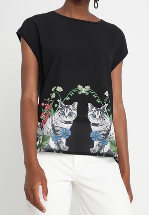 Haut noir à manches courtes avec un imprimé graphique de deux chats et des accents floraux en bleu et vert. Texture lisse et coupe décontractée.